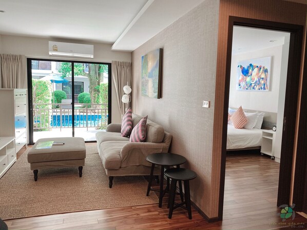 A hotel room with a sofa, a small table, a bed, and a view of a swimming pool.