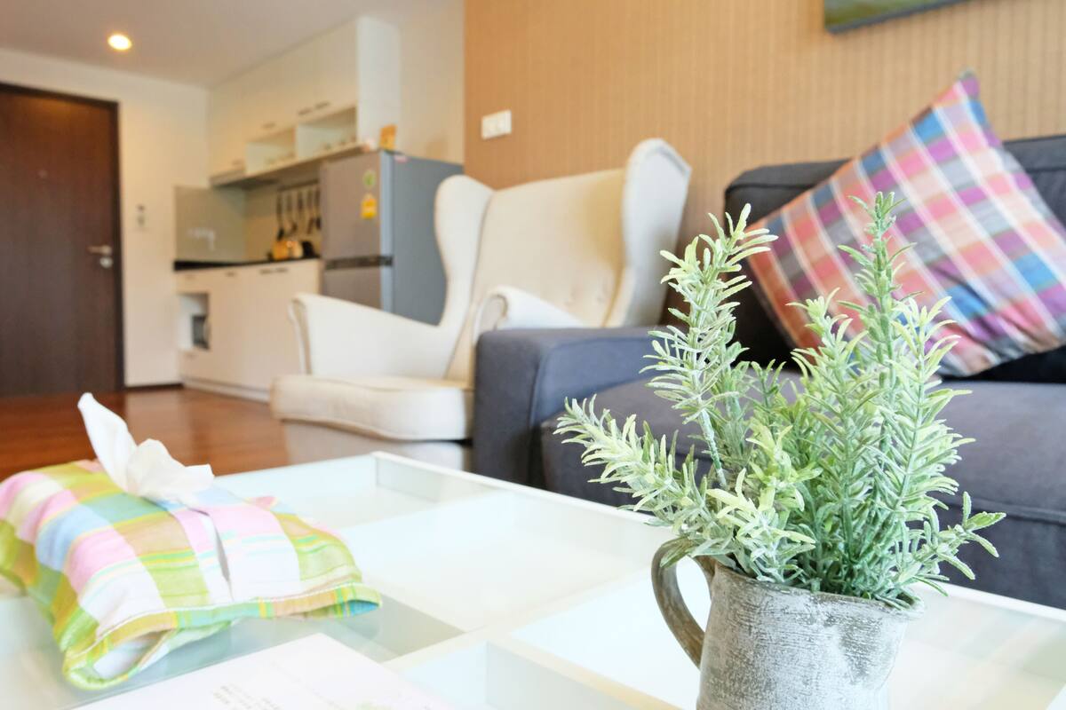 Uma sala de estar moderna com um sofá branco, um cobertor colorido sobre uma mesa de centro e um vaso com planta.