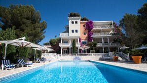 A swimming pool with lounge chairs, a white building with balconies, and surrounding trees. - Chambre d'hôtes La Potinière (Saint-Raphael)