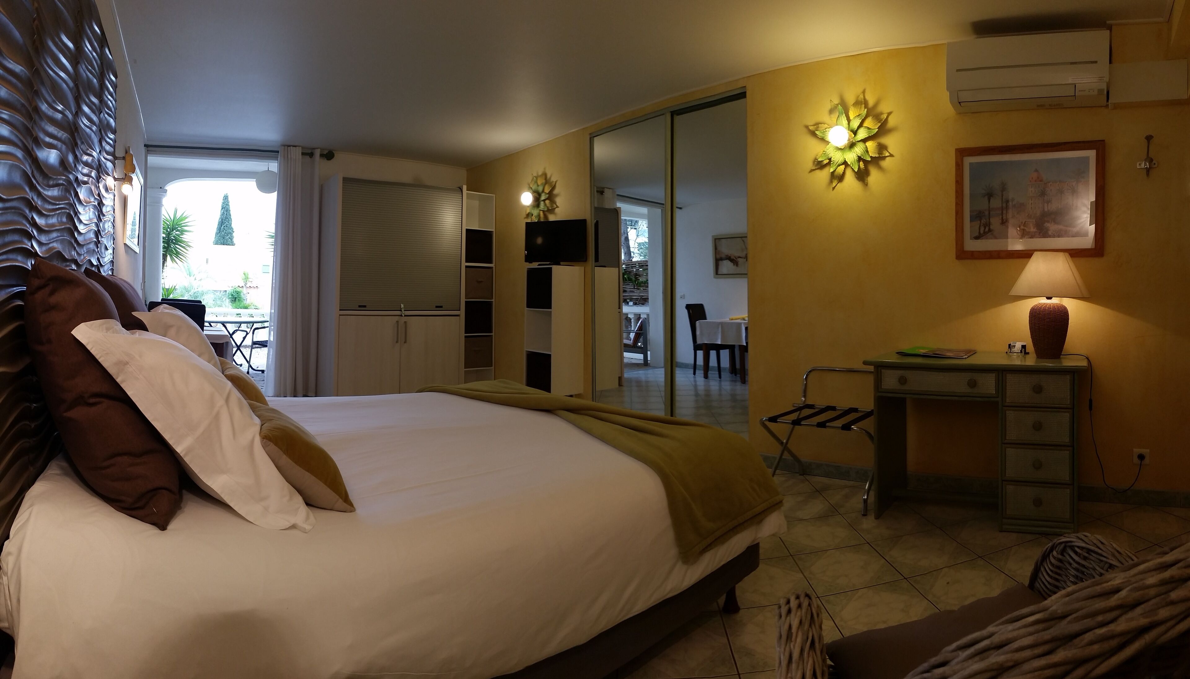 Una habitación de hotel con cama, escritorio, silla, lámpara y un cuadro en la pared.