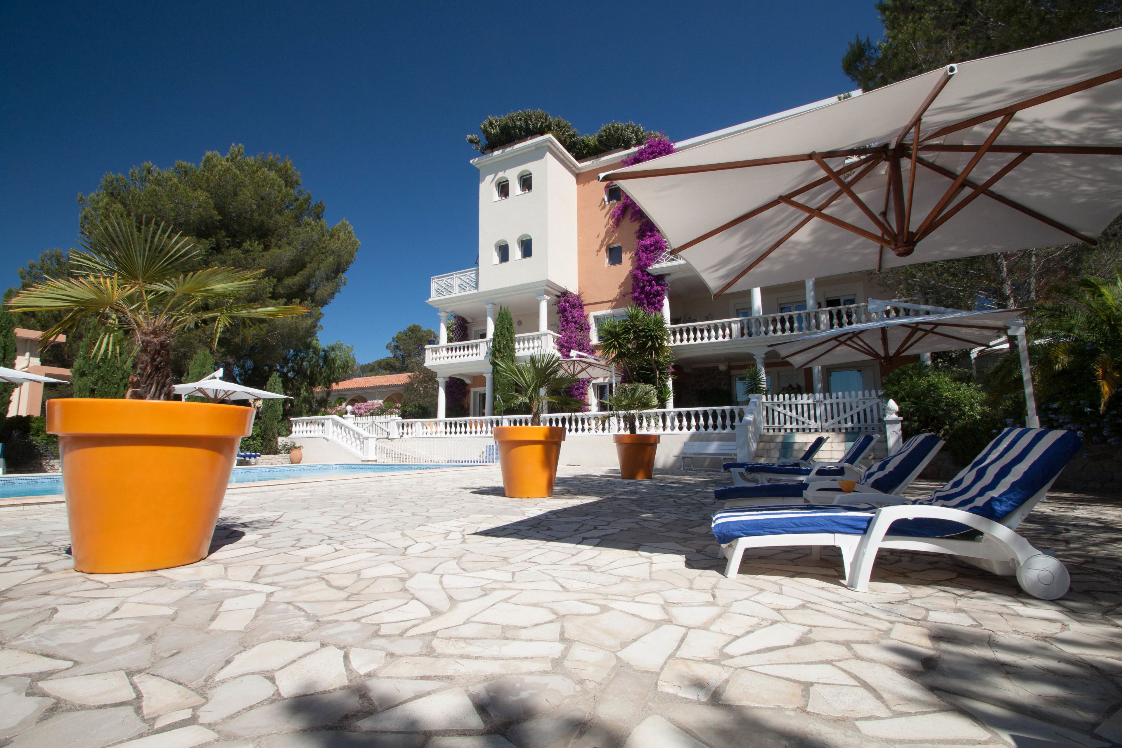 A poolside area with lounge chairs, umbrellas, and large potted plants.