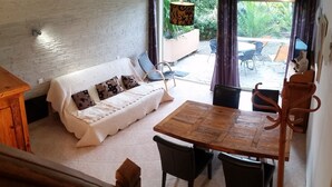 A cozy living area with a white sofa, wooden dining table, and chairs. A staircase leads to an upper level. - Chambre d'hôtes La Potinière (Saint-Raphael)