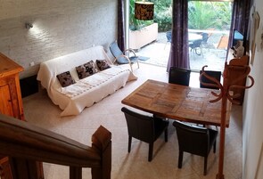 Un espacio de sala acogedor con un sofá blanco, una mesa de comedor de madera y sillas. Una escalera conduce a un nivel superior.