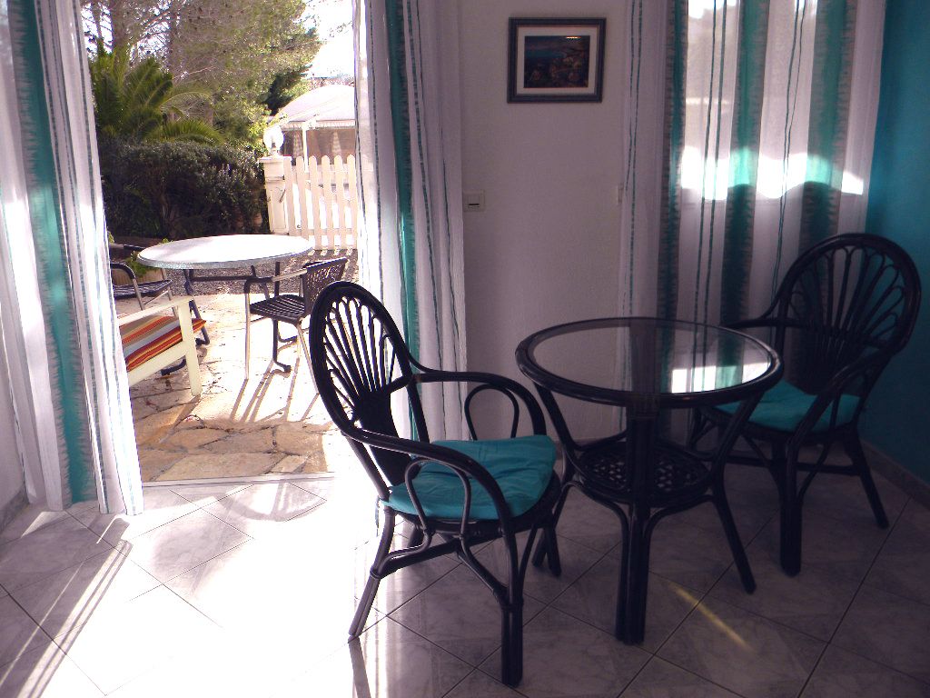 A patio with a round table and four chairs, a white fence, and a door with a picture on the wall.