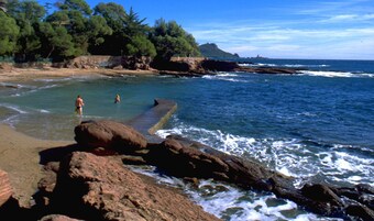 Una playa rocosa con agua cristalina, algunas personas y una isla distante.