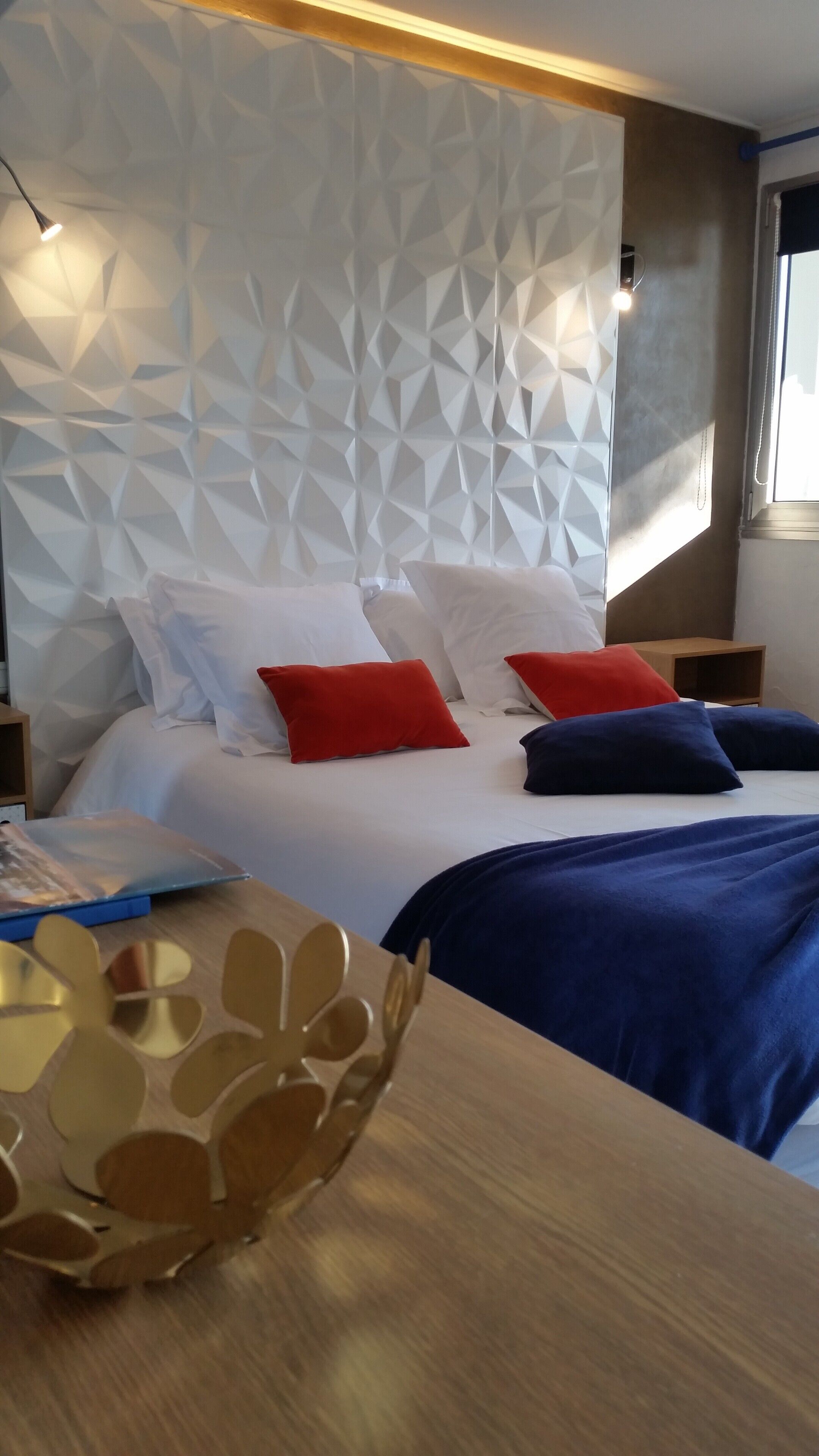 Camera da letto moderna con una testiera a motivi geometrici, un comodino in legno e una copripiumone blu.