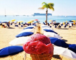 Escena de playa con una bola de helado rojo en primer plano y sombrillas de playa al fondo.