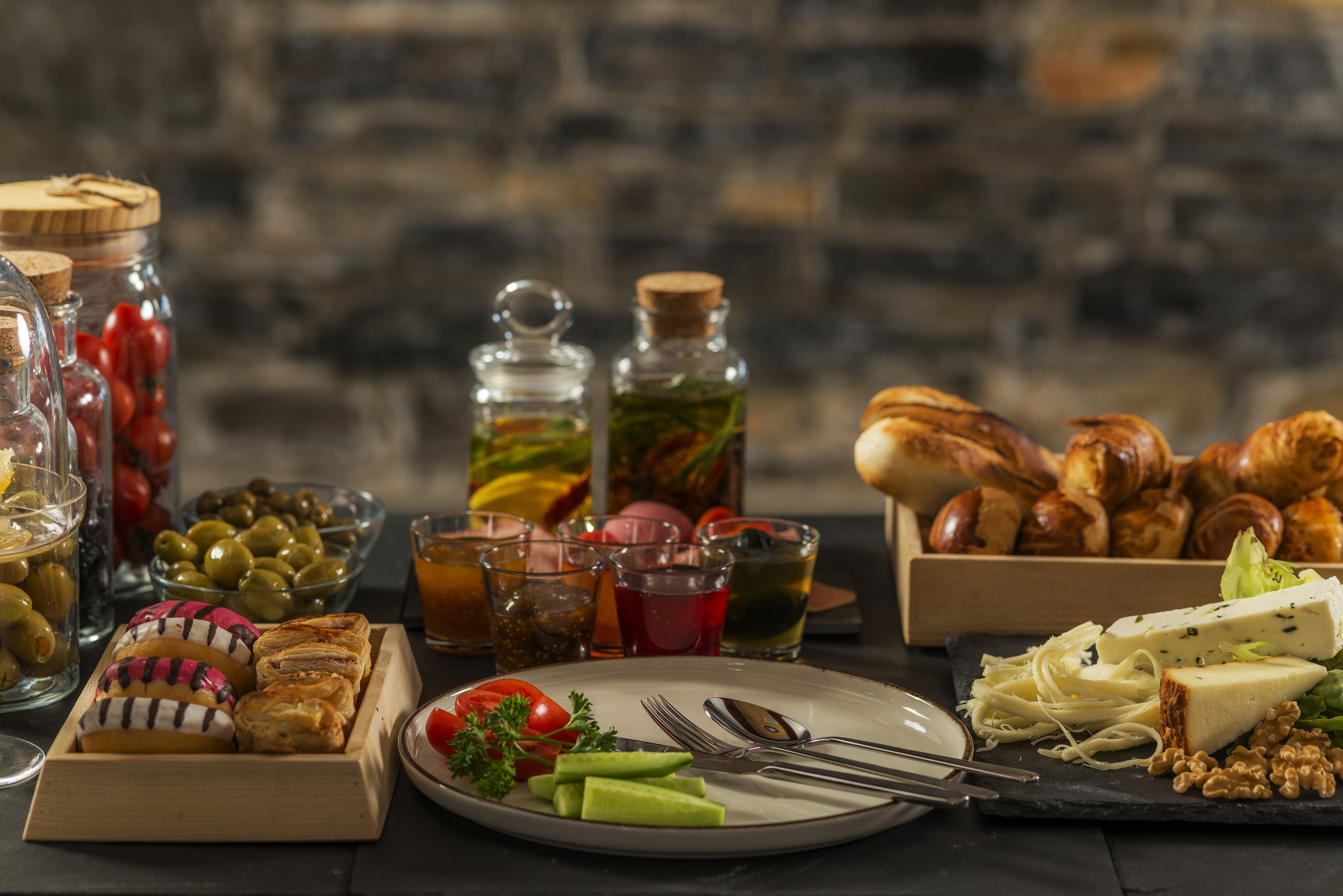 A variety of food items including pastries, cheese, and olives on a table with a stone wall background.