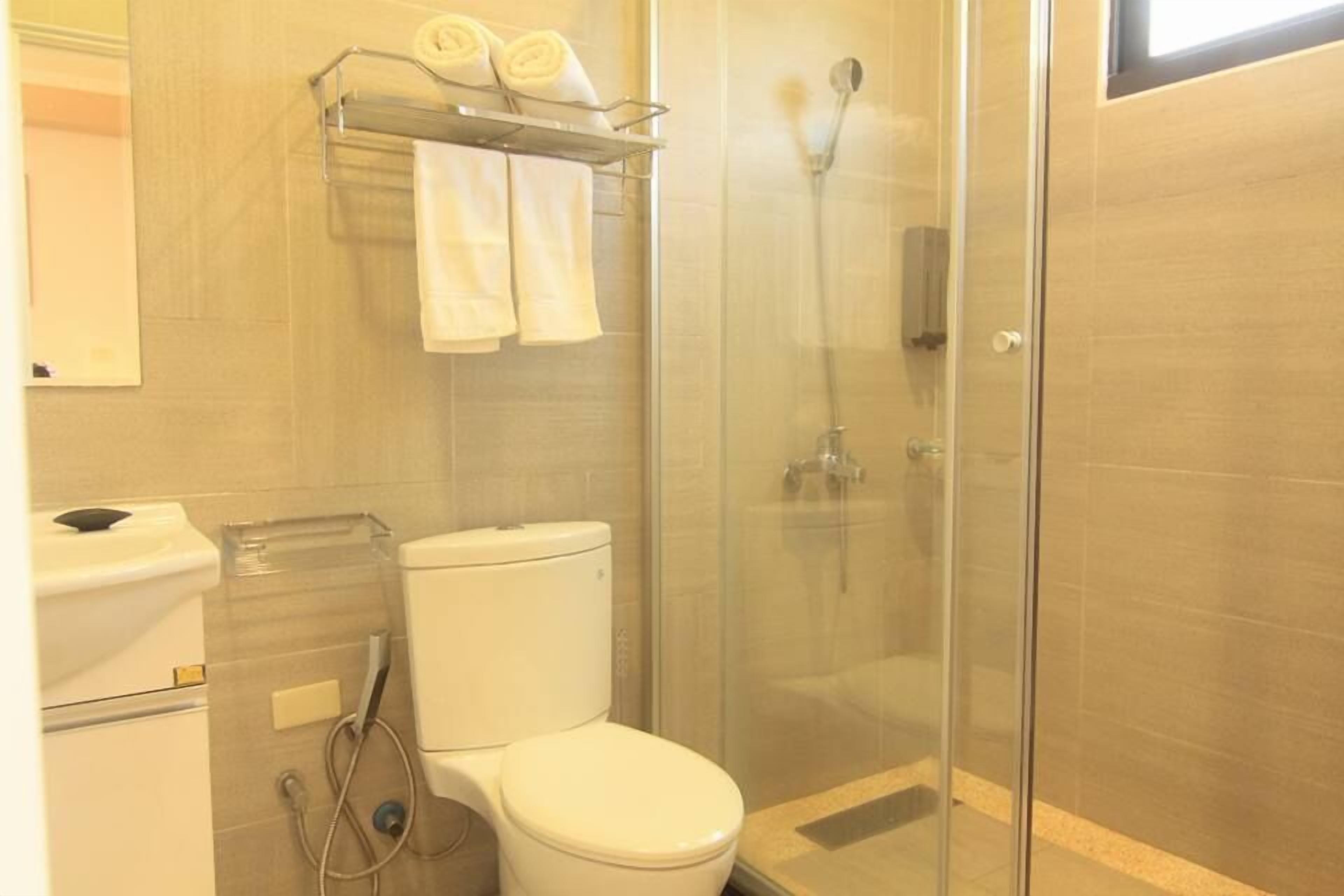 Ein Badezimmer mit Toilette, einer Duschkabine und einem Handtuchhalter mit aufgerollten Handtüchern.
