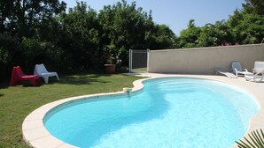 A swimming pool with a curved edge, surrounded by a grassy area and a few lounge chairs. - Chez Elise et Gabriel (Mirmande)
