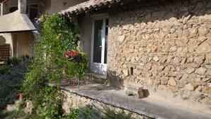 A stone building with a tiled roof, a balcony, and a potted plant with flowers. - Chez Elise et Gabriel (Mirmande)