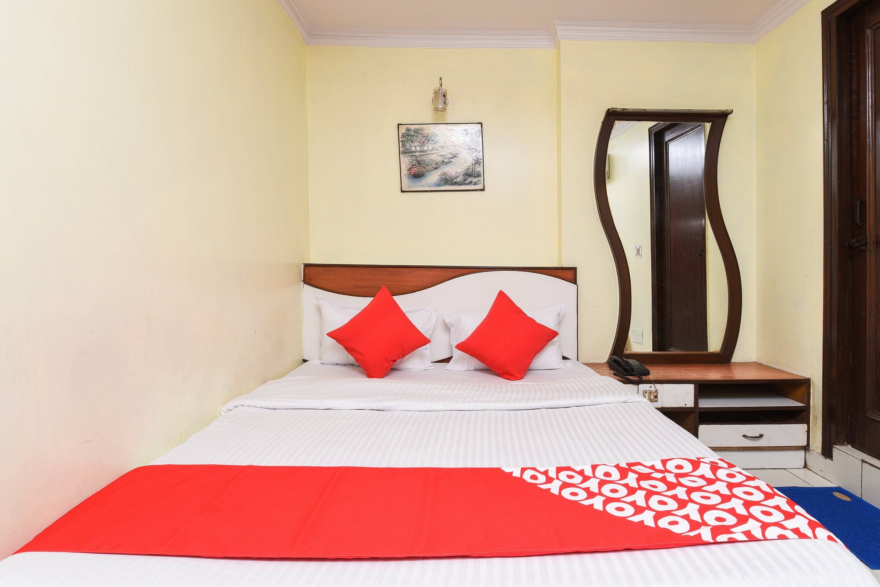 A neatly made bed with red and white bedding, a bedside table with a lamp, and a mirror on the wall.