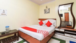 Habitación de hotel con cama, mesita de noche, espejo y una pequeña mesa con jarras y vasos.
