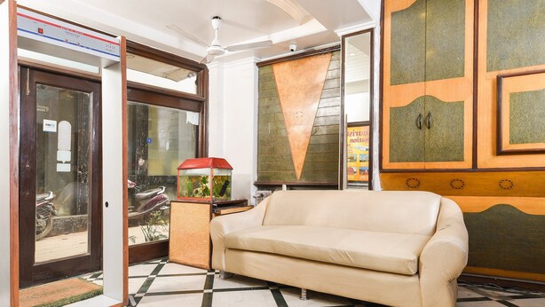 Un vestíbulo de hotel con piso a cuadros, un sofá color beige, un acuario y una puerta con panel de vidrio.
