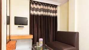 Una sala de estar con un sofá marrón, una mesa de centro de vidrio, un televisor de pantalla plana y una cortina con estampado a rayas.