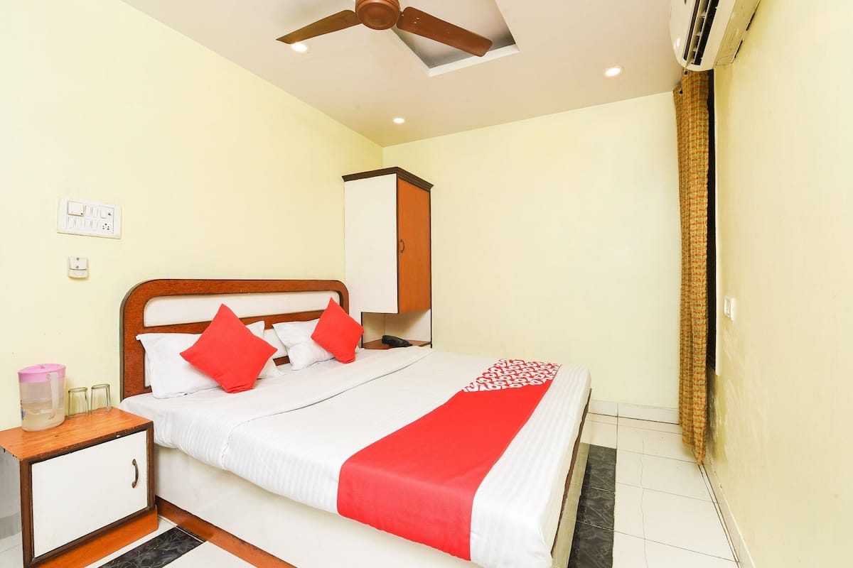 A neatly made bed with a red and white bedspread, a wooden nightstand with a small cabinet, and a ceiling fan.