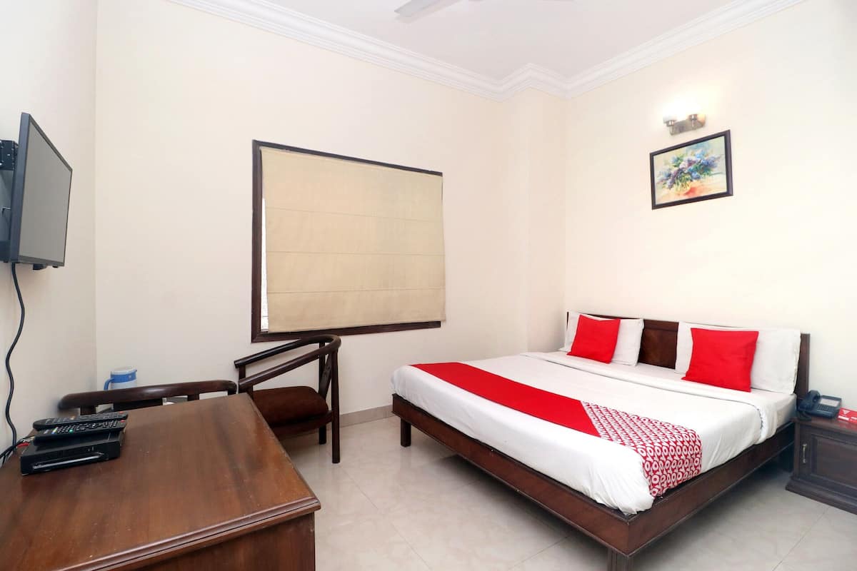 Una habitación de hotel con cama, escritorio, silla, televisión y un cuadro en la pared.
