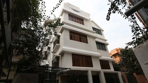 A multi-story residential building with a white facade, large windows, and a gated entrance.