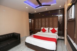 Una habitación de hotel con cama, ventilador de techo, sofá de cuero negro y ventana con persianas.