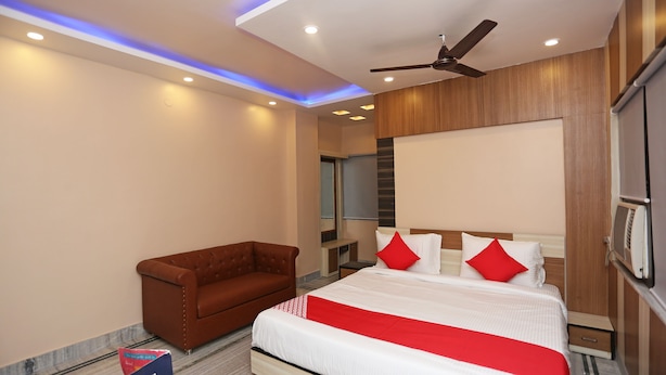 A modern hotel room with a large bed, a brown armchair, and a ceiling fan.