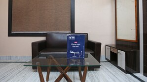 A hotel lobby with a glass table, a brown leather sofa, a wall-mounted bulletin board, and a cabinet with drawers.