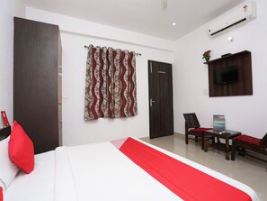 A hotel room with a bed, a TV mounted on the wall, a desk with a chair, and a window with curtains. - OYO 19535 Hotel Taj Niwas (Agra)