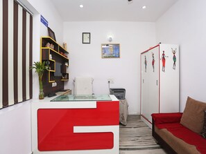 A modern living room with a red and white sofa, a small table, a bookshelf, and a door with artwork. - OYO 19535 Hotel Taj Niwas (Agra)