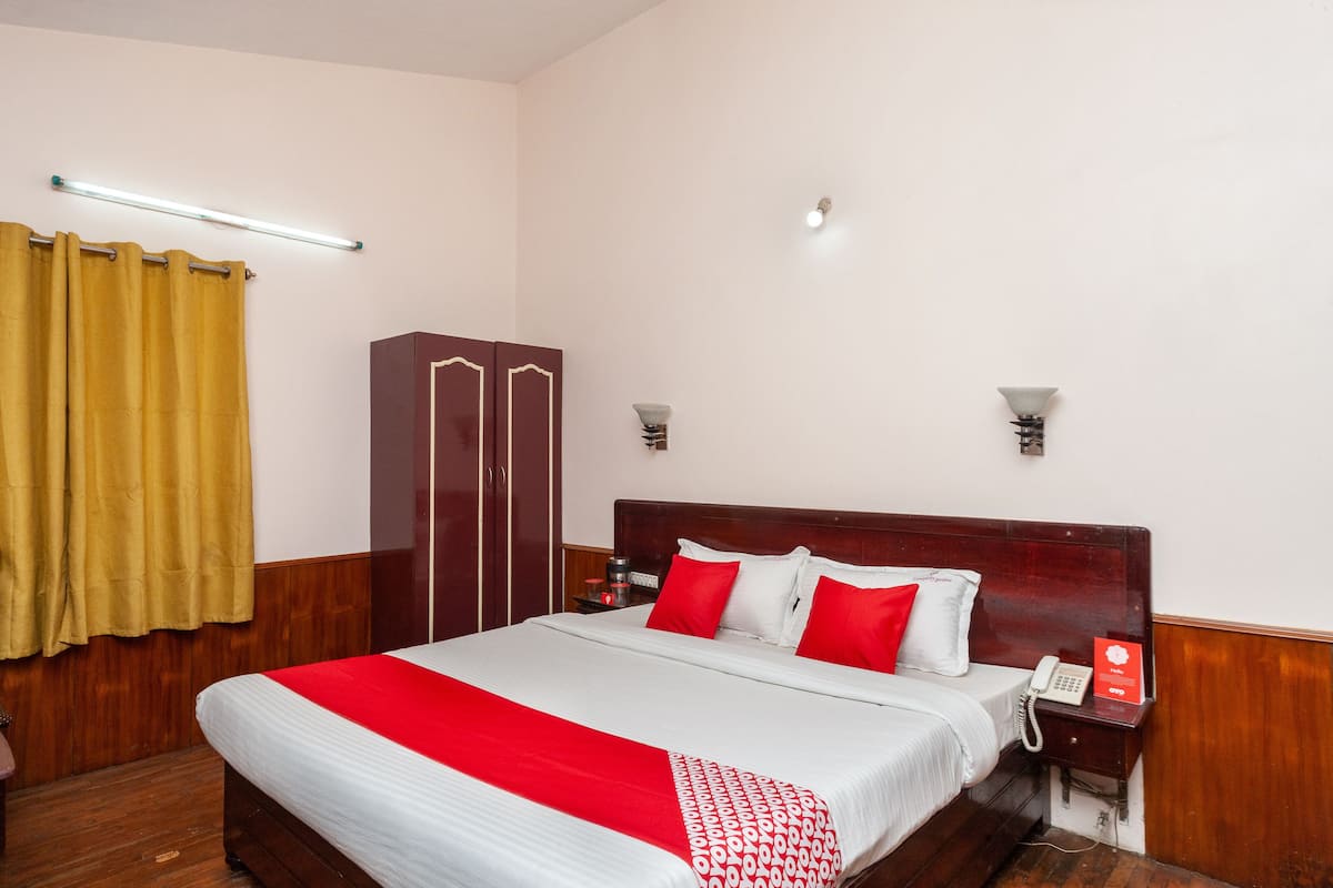 A hotel room with a large bed, wooden wardrobe, bedside table with a lamp, and a telephone.