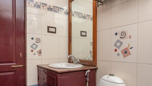 A bathroom with a white toilet, a wooden cabinet with a sink, a mirror, and a towel rack. - OYO 27809 Hotel Ganapathy Garden (Kodaikanal)