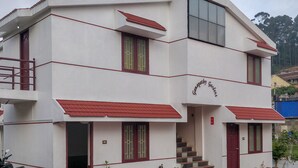 A multi-story building with a red roof and white walls, featuring a staircase and a sign that reads "Gardeny Gardens." - OYO 27809 Hotel Ganapathy Garden (Kodaikanal)