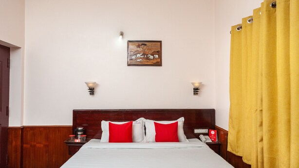 A hotel room with a wooden headboard, a bed with red and white bedding, a wall-mounted telephone, and a yellow curtain. - OYO 27809 Hotel Ganapathy Garden (Kodaikanal)