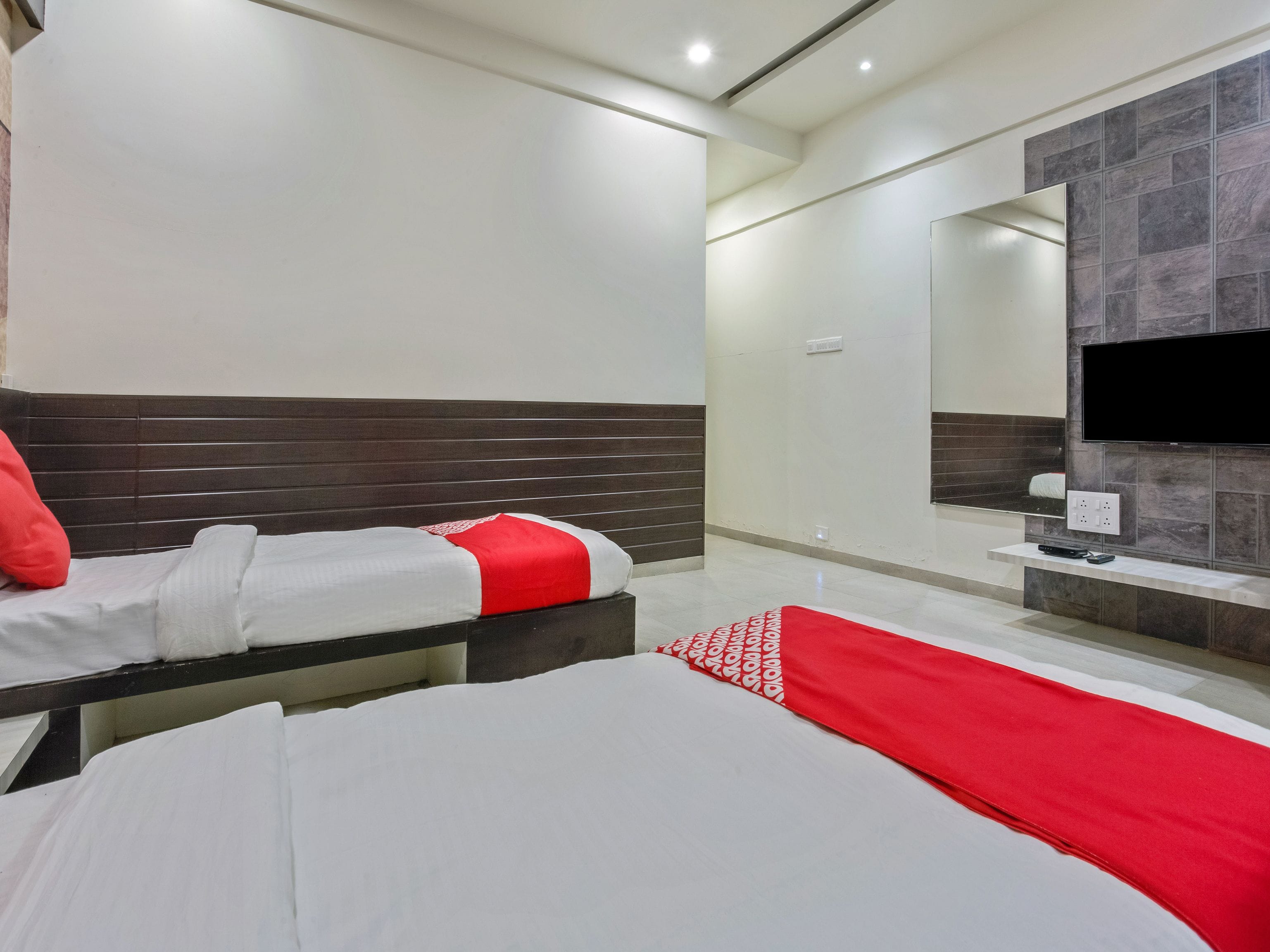 Habitación de hotel con dos camas, televisión y baño con espejo y paredes de azulejos.