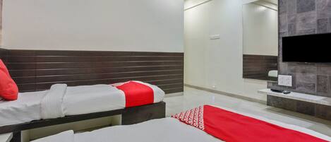 Habitación de hotel con dos camas, televisión y baño con espejo y paredes de azulejos.