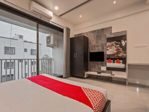 Une chambre moderne avec un grand lit, un téléviseur fixé au mur et un balcon offrant une vue sur les immeubles.