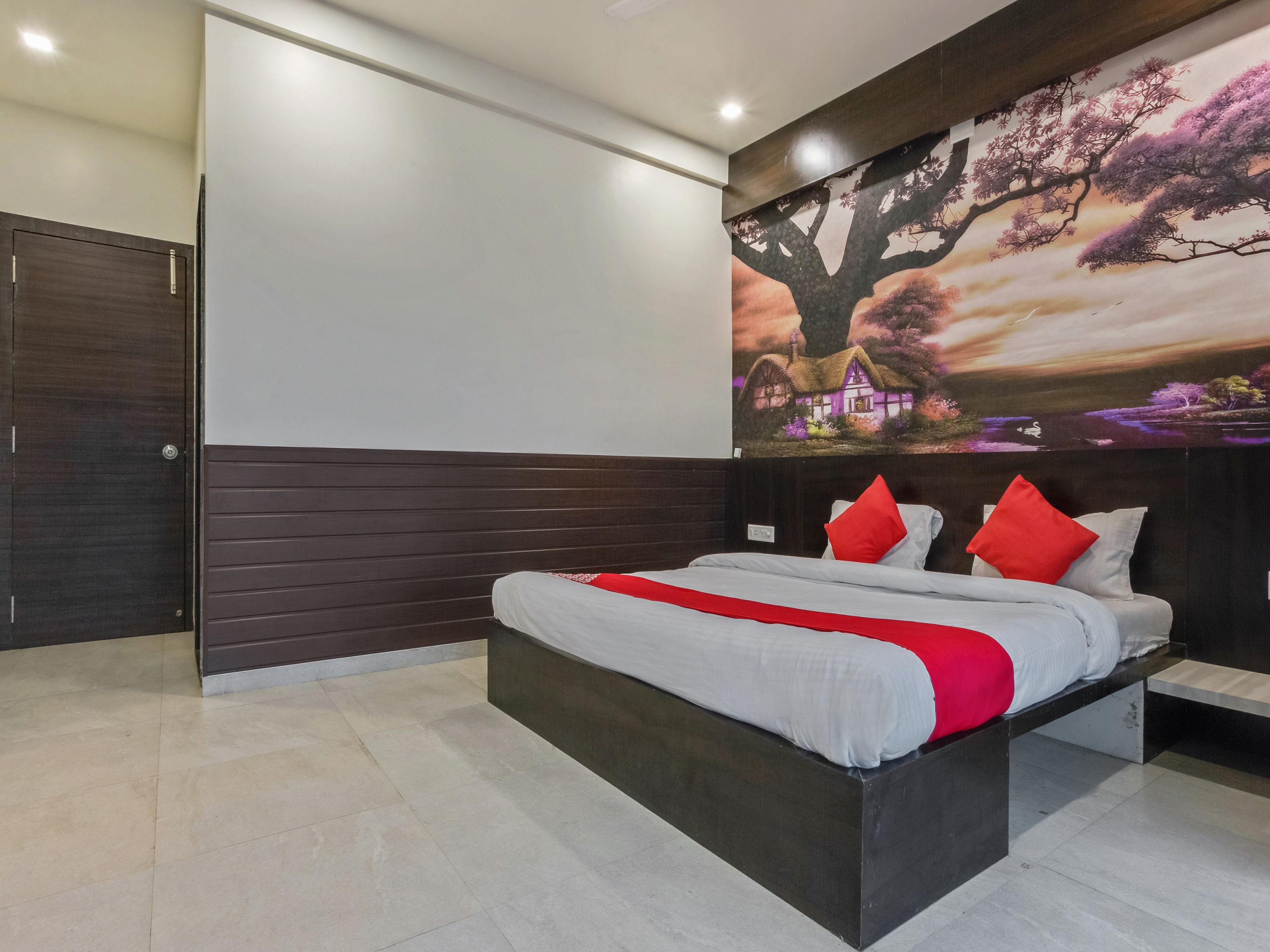 Quarto moderno com uma cama grande, painéis de madeira escura e um mural de uma árvore e uma casa.