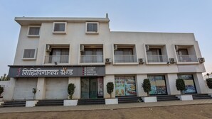 Un edificio de varios pisos con un letrero que indica 'Siddhivinayak Brand', ofreciendo servicios como restaurante con aire acondicionado, alojamiento con aire acondicionado, salón de conferencias con aire acondicionado y salón de banquetes con aire acondicionado.