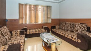Una sala de estar con sofás estampados, una mesa de centro de vidrio y una ventana con persianas.