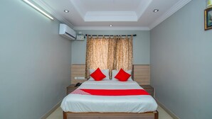 Una cama bien hecha con colcha roja y blanca, cabecera de madera y lámpara en el techo.