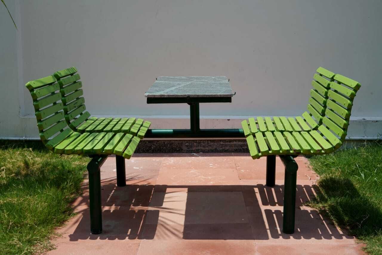 Twee groene parkbanken met een kleine tafel ertussen, voor een effen muur.