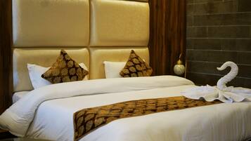 A hotel room with a large padded headboard, two white beds with matching pillows, and a decorative towel on the bed.