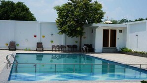 Piscina com deck revestido, rodeada por cadeiras e uma parede branca.