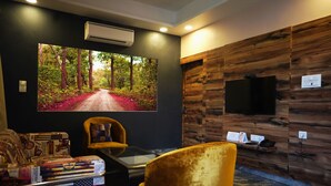 Quarto moderno com uma televisão grande na parede, um painel de parede em madeira e um espaço de estar com uma poltrona amarela e uma mesa.