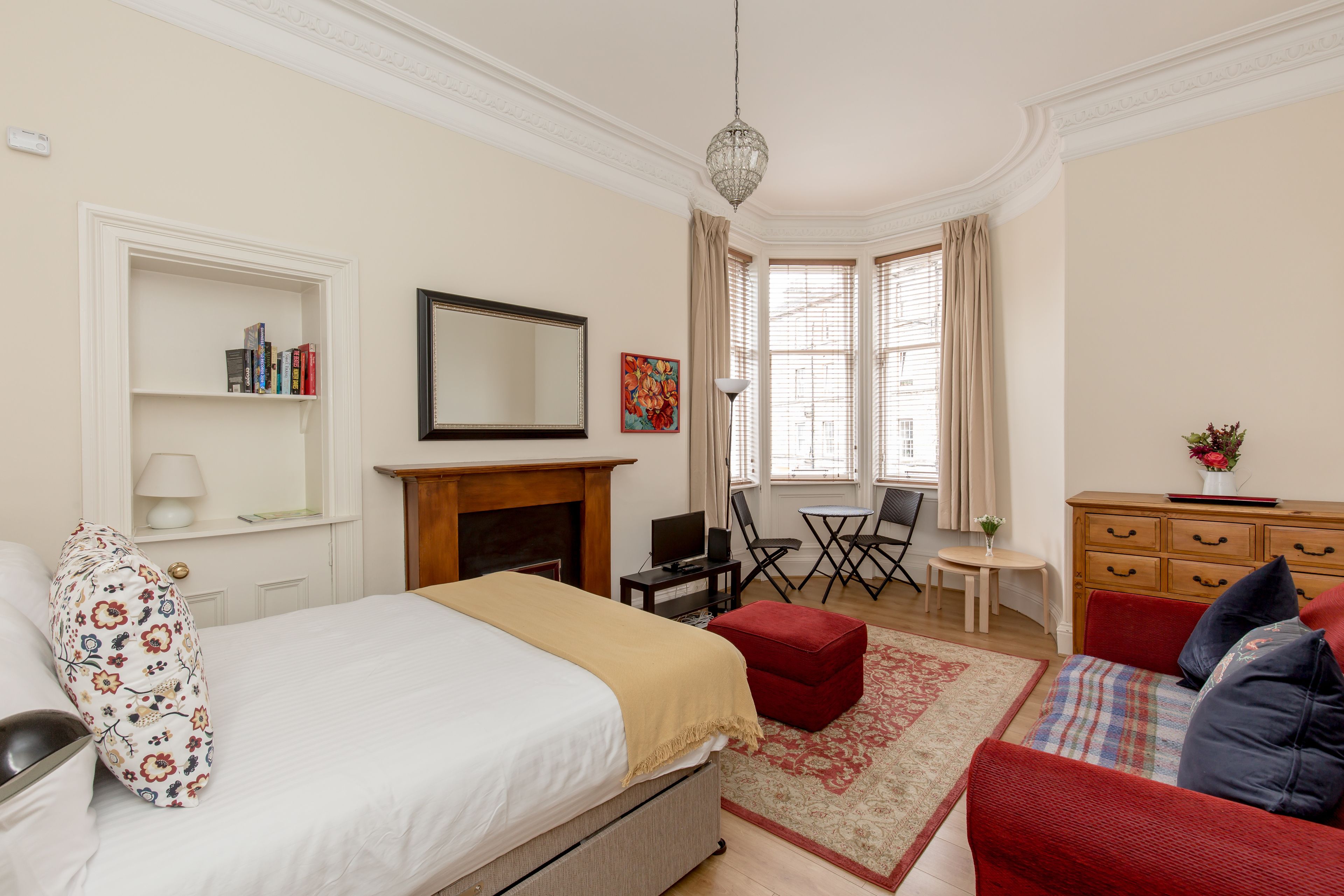 A hotel room with a bed, a red sofa, a fireplace, a desk, and a window with curtains.