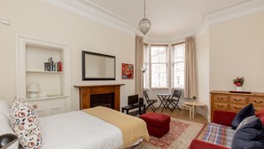 A hotel room with a bed, a red sofa, a fireplace, a desk, and a window with curtains. - Silver Lining Lochrin Terrace Apartment (Edinburgh)