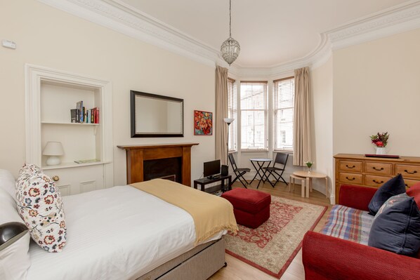 A hotel room with a bed, a red sofa, a fireplace, a desk, and a window with curtains. - Silver Lining Lochrin Terrace Apartment (Edinburgh)