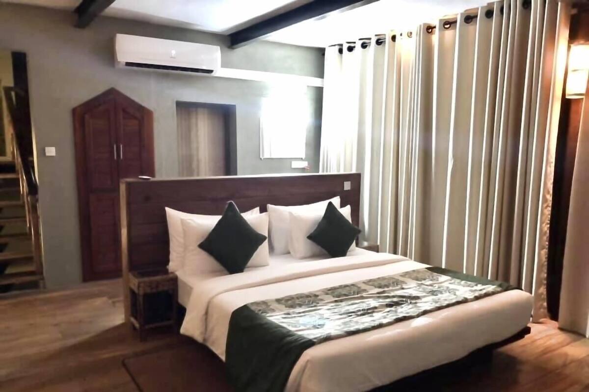 A bedroom with a bed, a nightstand, a wardrobe, and a window with curtains.