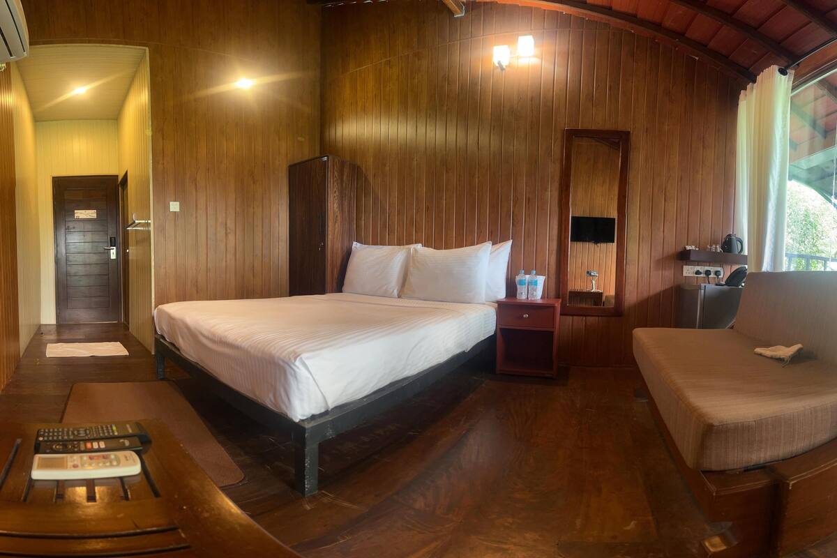 A wooden-floored room with a bed, bedside table, and a sofa.