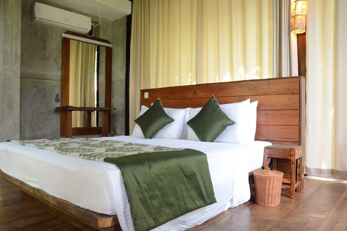 A neatly made bed with a wooden headboard, a green throw blanket, and two green pillows.