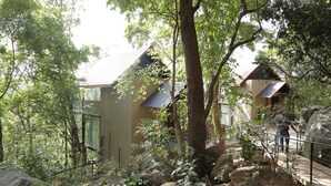A building with a sloped roof, surrounded by trees and rocks. - Arangala Forest Lodge (Naula)