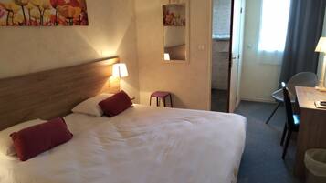 Quarto de hotel com uma cama grande, uma escrivaninha com cadeira, um banquinho pequeno, um espelho e um quadro na parede.